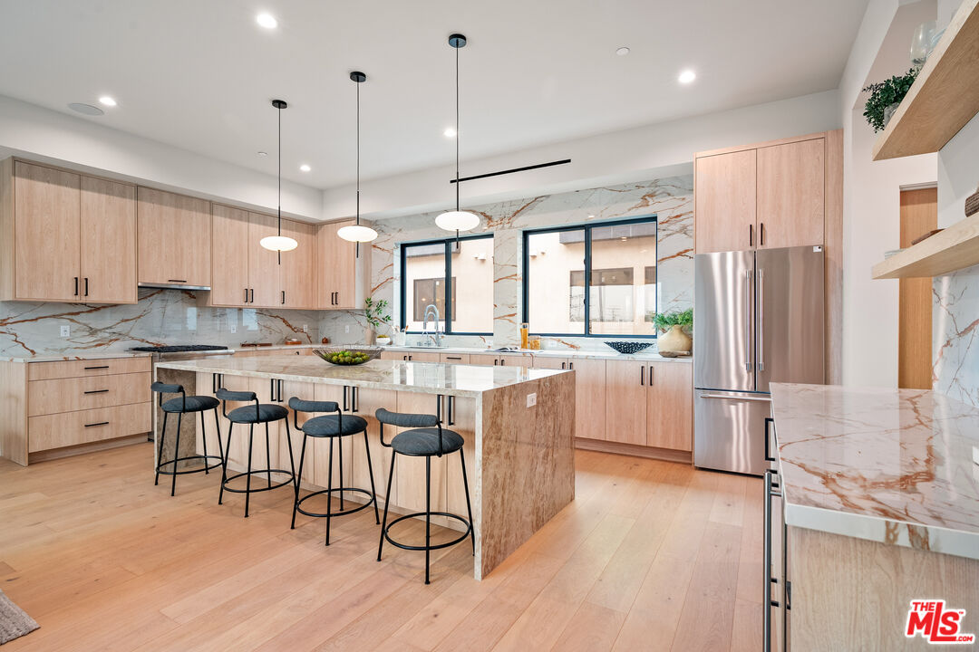Modern kitchen with a marble island, light wood cabinets, stainless steel appliances, and four bar stools.