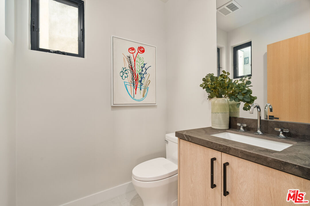 Bathroom with a light wood vanity, dark stone counter, and framed colorful floral artwork.