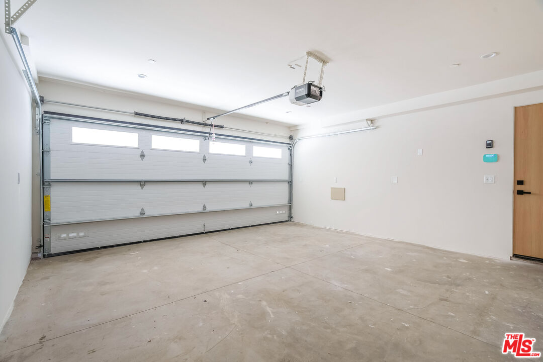 Empty garage with a wide windowed door, ceiling-mounted opener, and bare concrete floor.