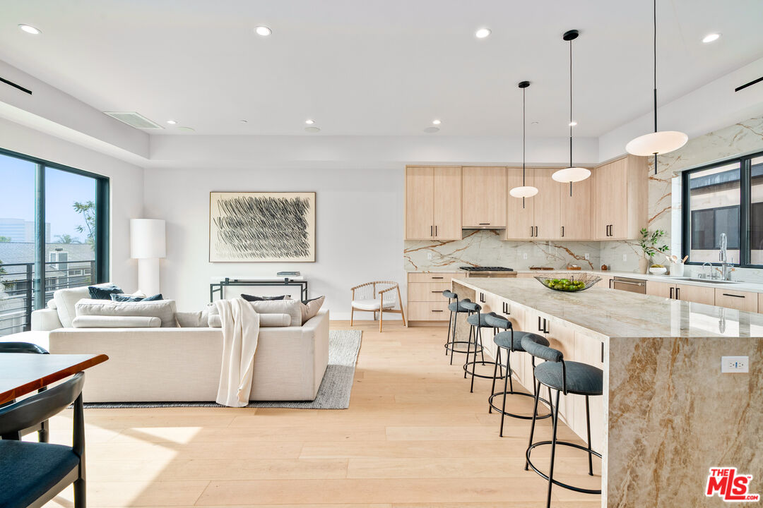 Open-plan kitchen and living room with a marble island, pale wood cabinetry, and balcony doors.