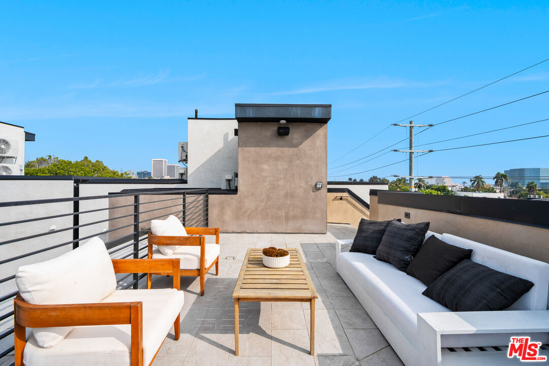 Furnished rooftop terrace with white sofas, wooden lounge chairs, and distant city views.