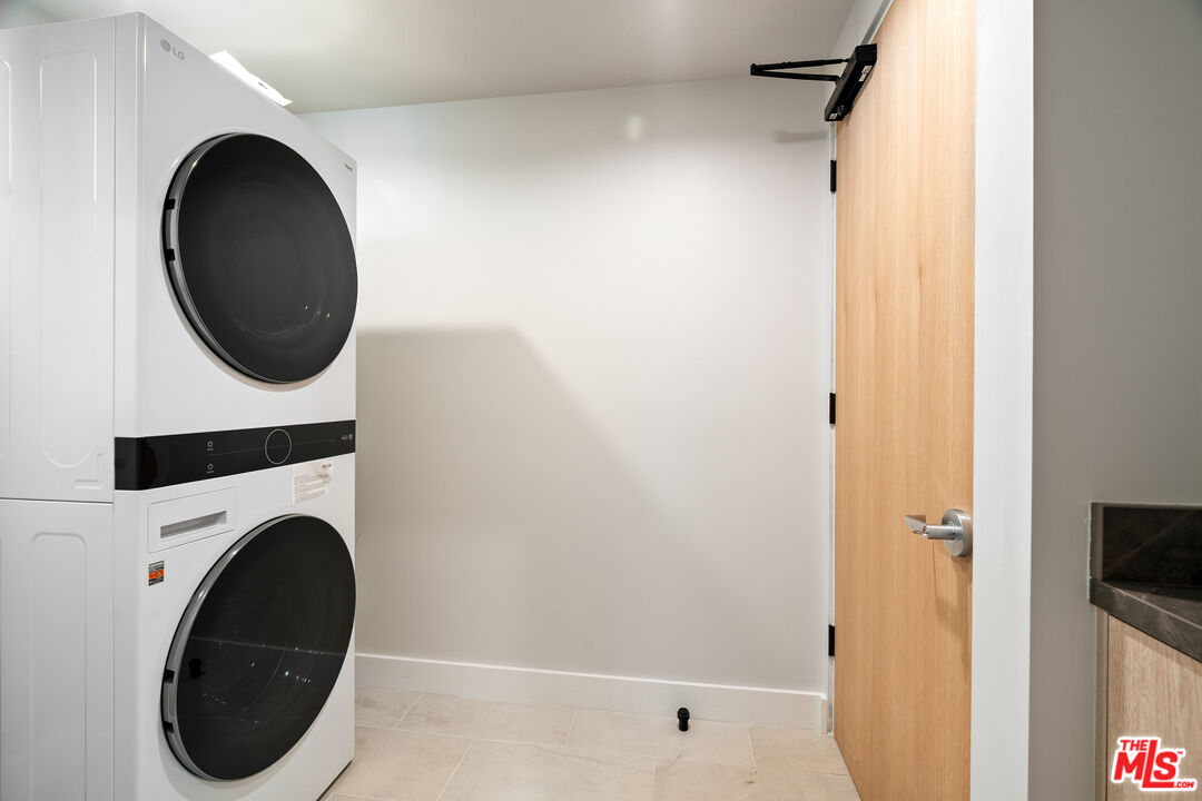Laundry room with a stacked washer and dryer beside an open wood door.