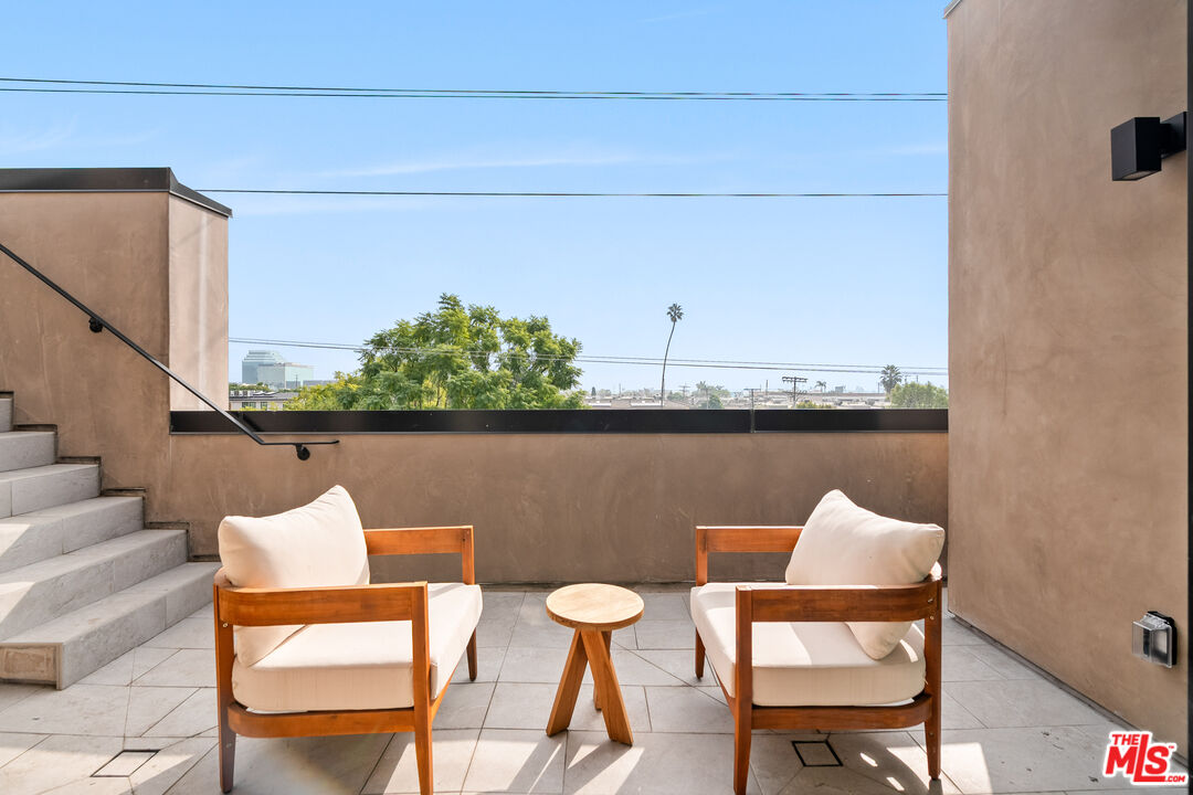 Rooftop patio with cushioned chairs, a small table, and a view of the city.