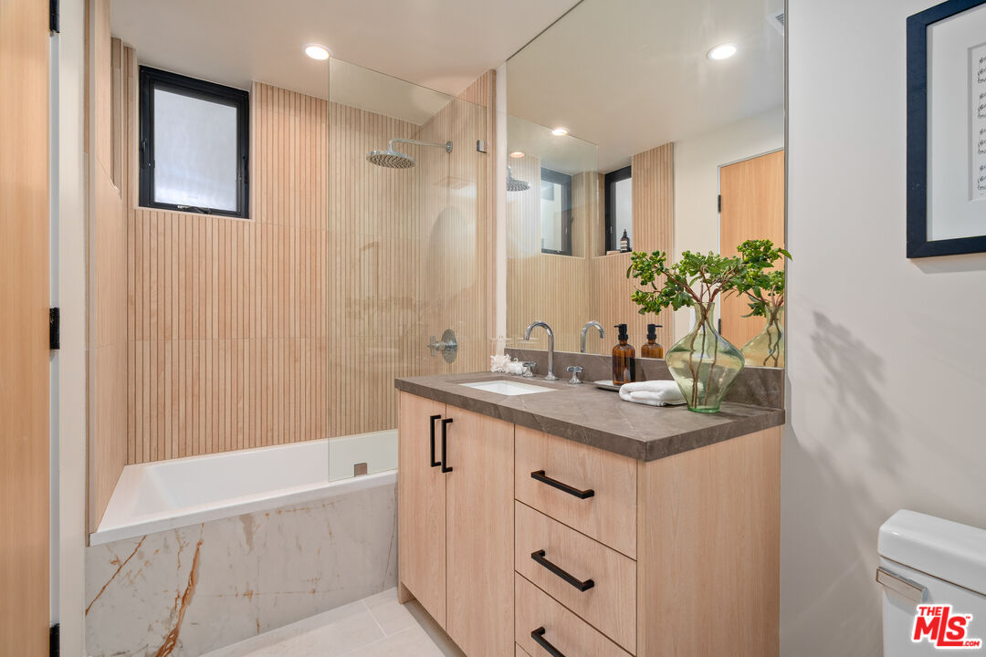 Bathroom with a wood-slat shower wall, glass enclosure, and light wood vanity.