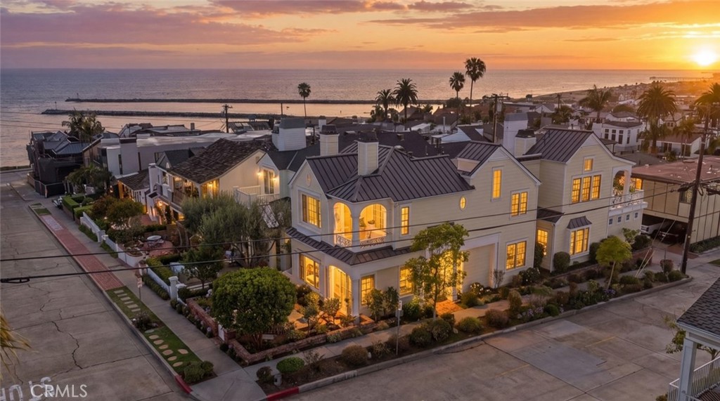 White multi-story coastal building with dark metal roofs and landscaped grounds at sunset.