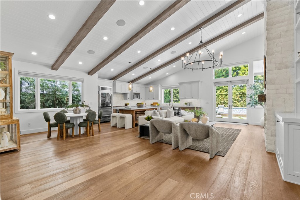 Open-plan kitchen and living area with exposed wood beams, dining table, and glass doors to greenery.