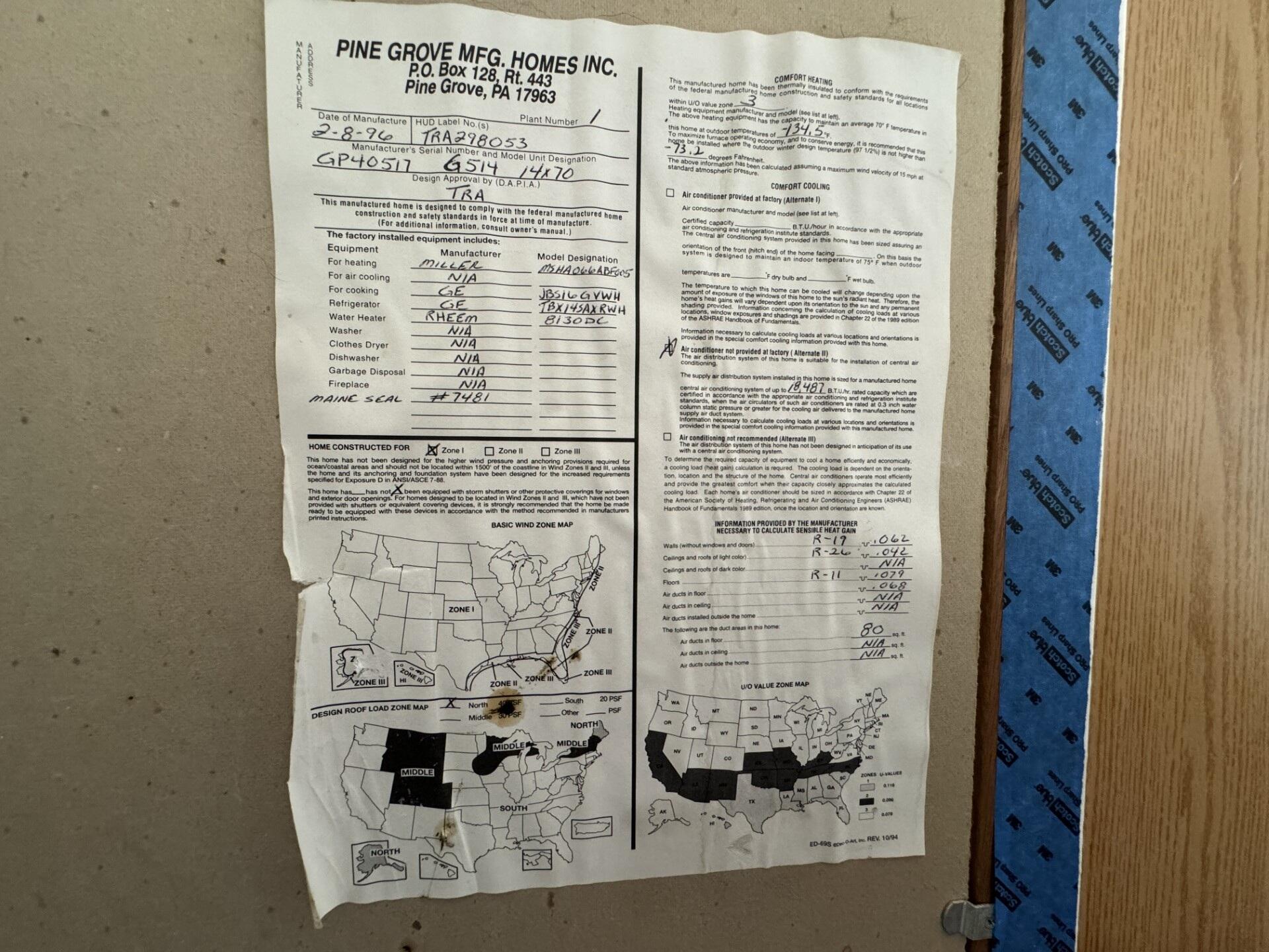 Manufactured-home certification sheet on an unfinished wall beside exposed insulation and wood framing.