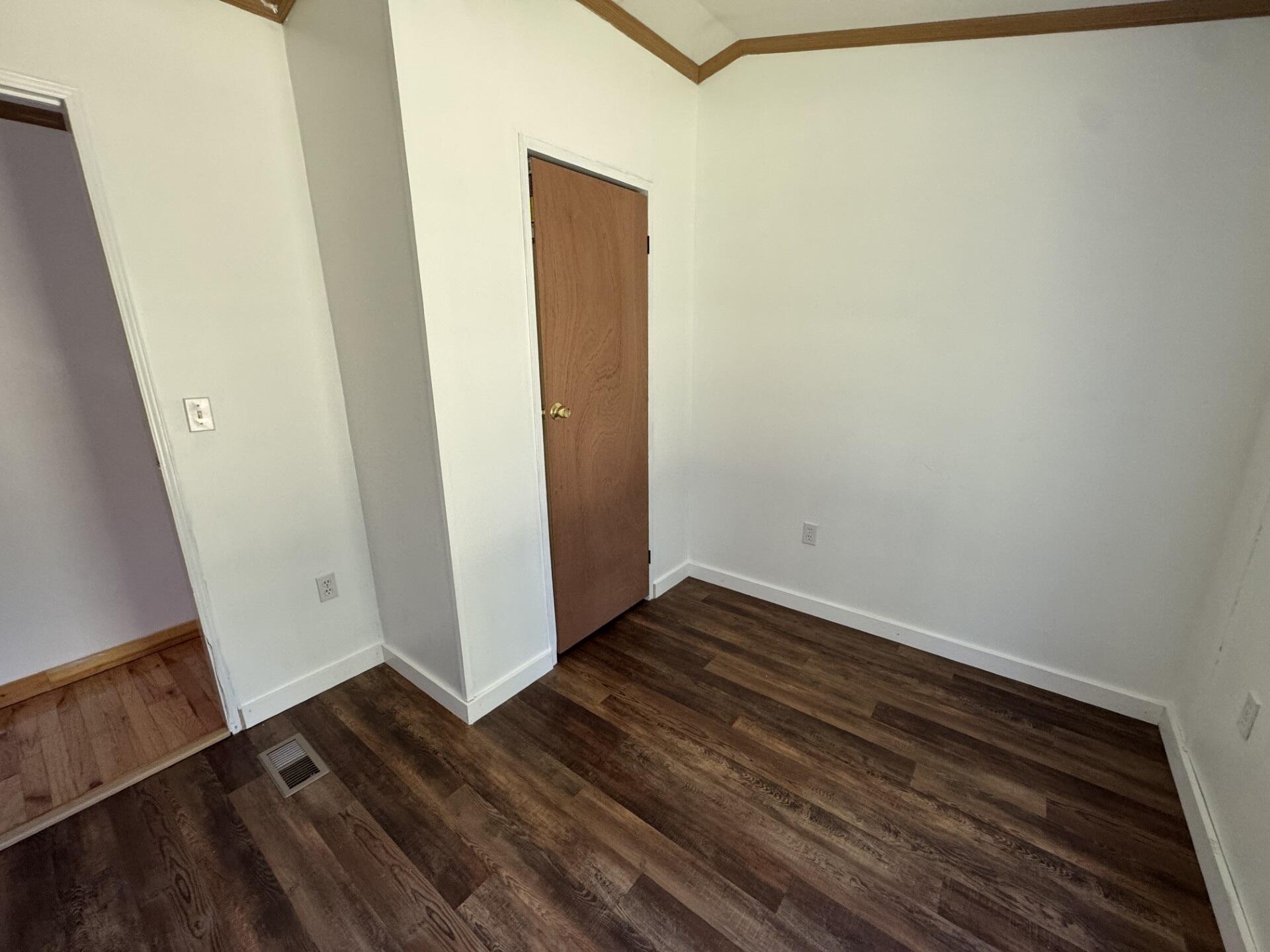 Empty room with dark wood-look floors, white walls, and a closed wooden door.
