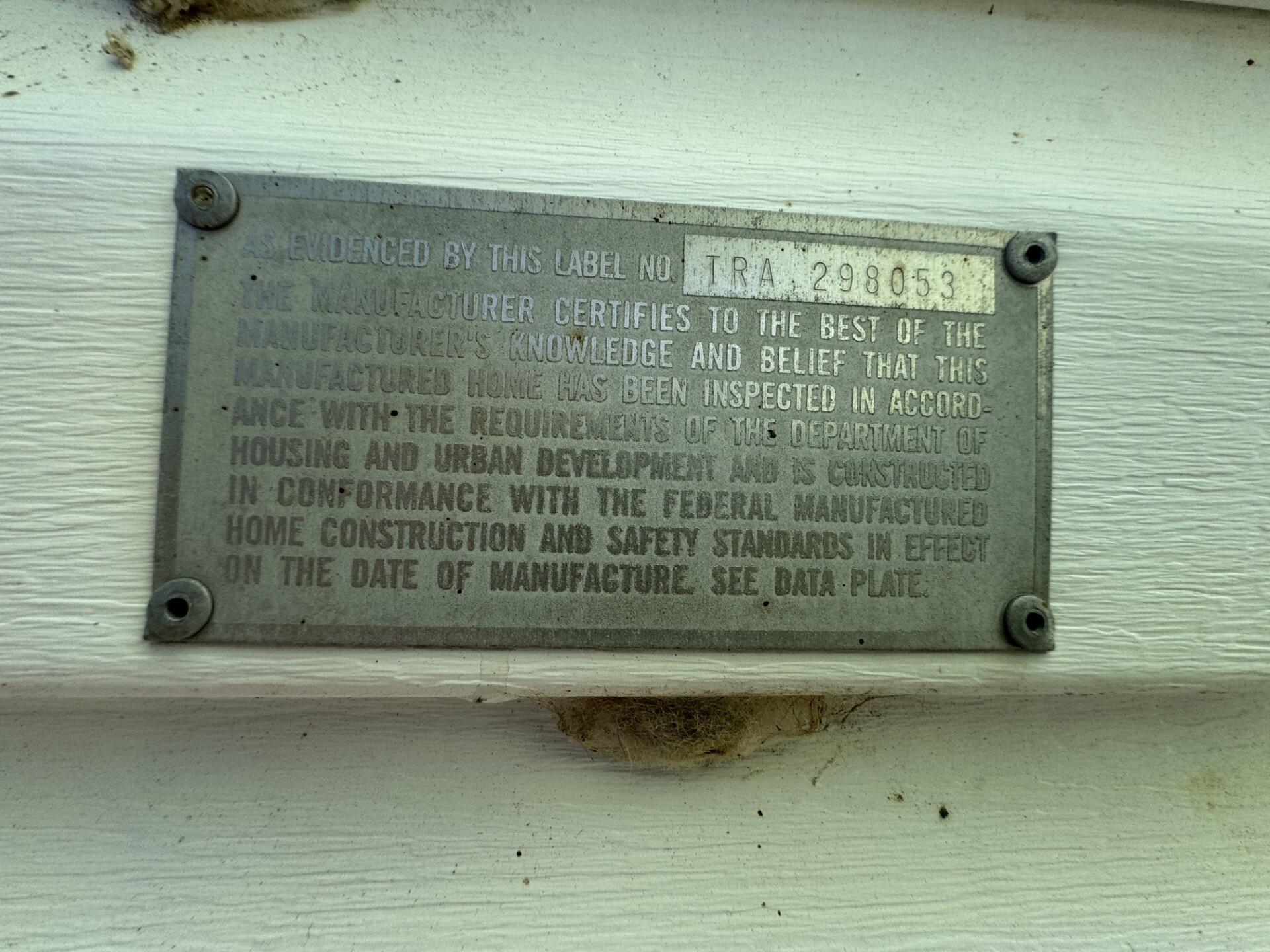 Manufactured-home certification label with serial number TRA 298053 on white exterior siding.