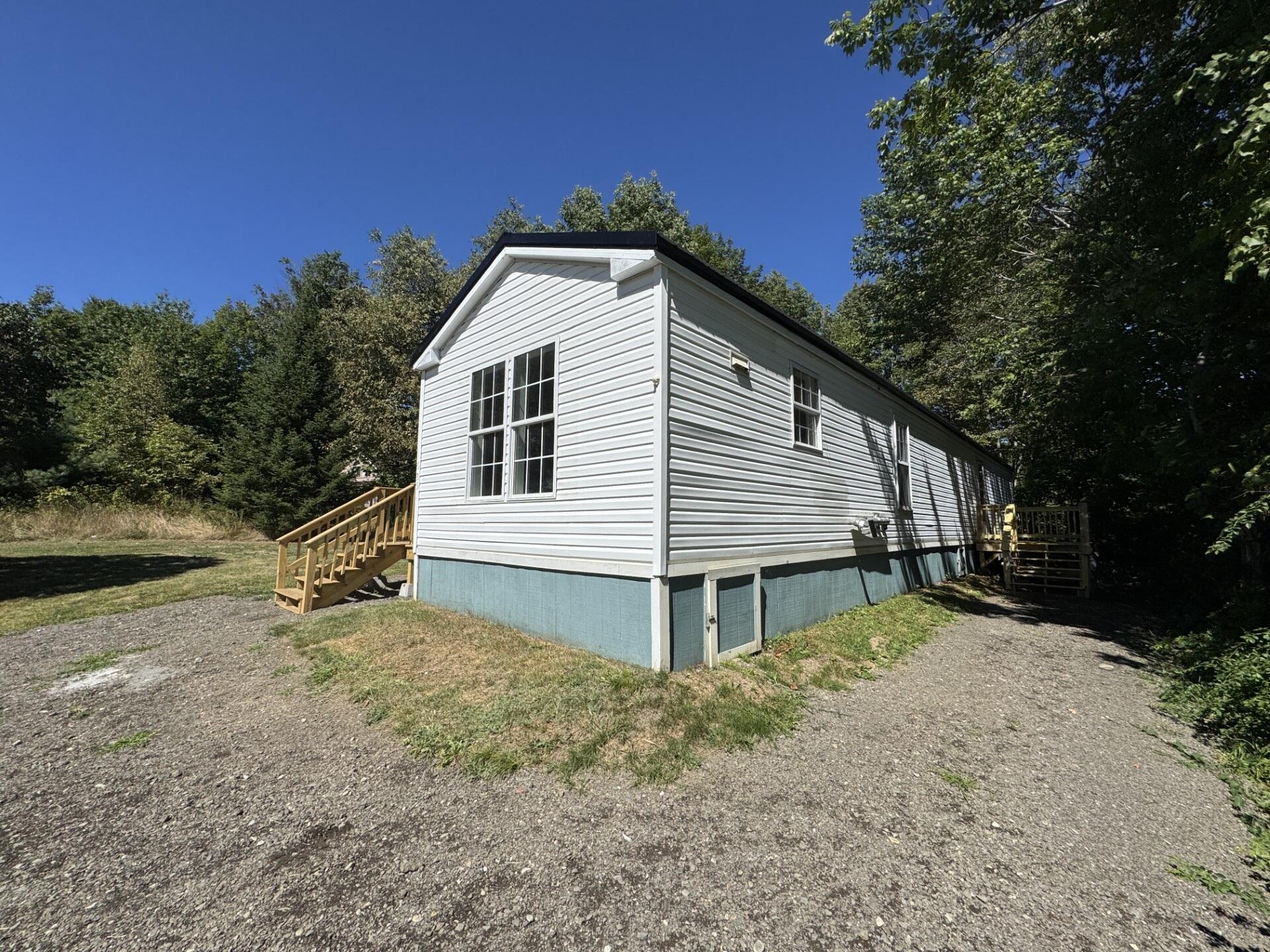 White-sided single-story home with wooden steps, blue-green foundation skirting, and a gravel drive.