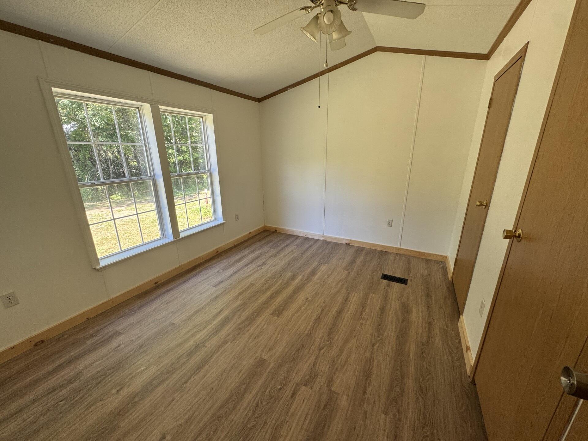 Empty room with wood-look flooring, two large windows, and a ceiling fan.