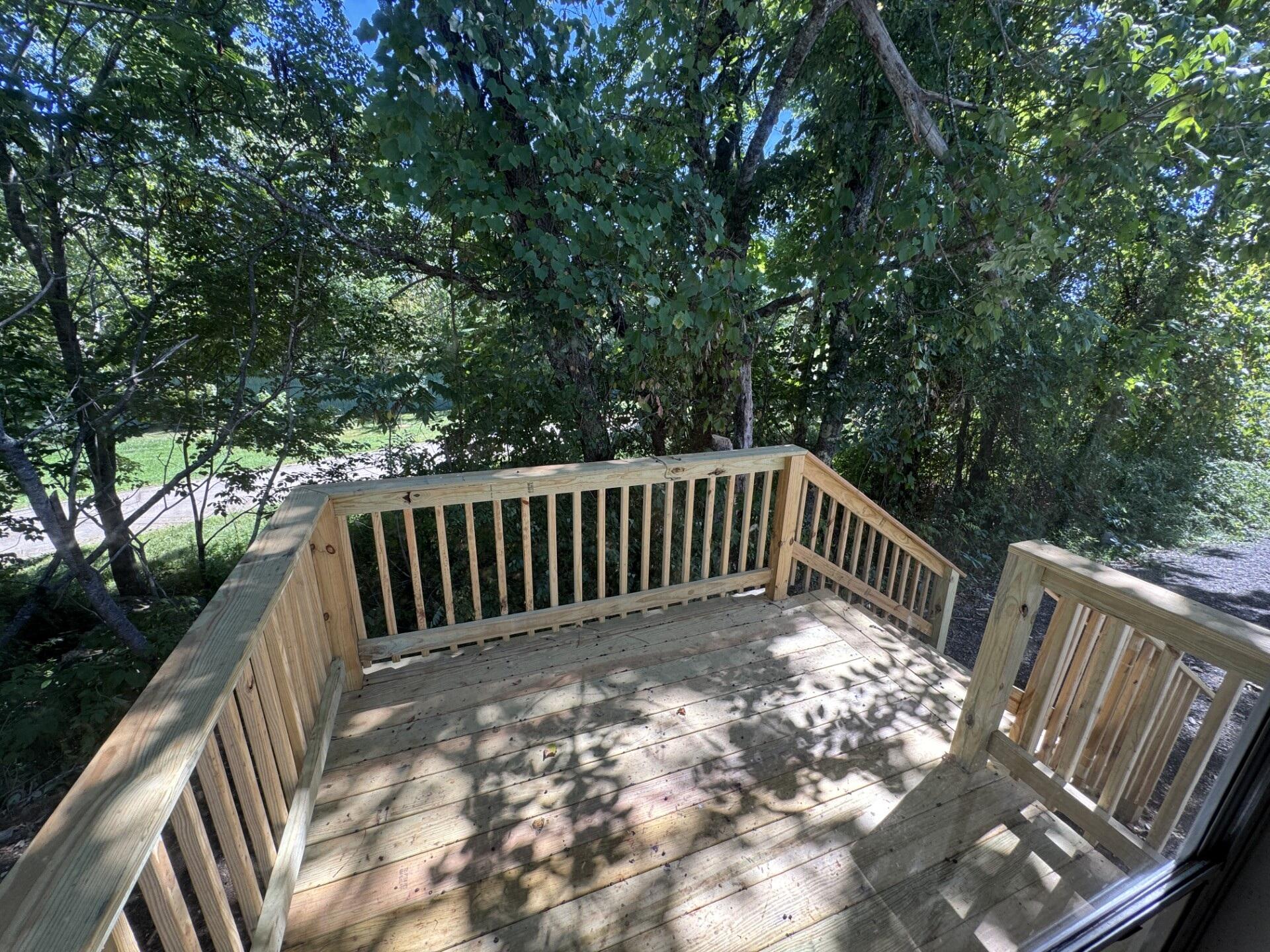 Wooden deck and steps shaded by leafy trees, with a gravel drive visible beyond.