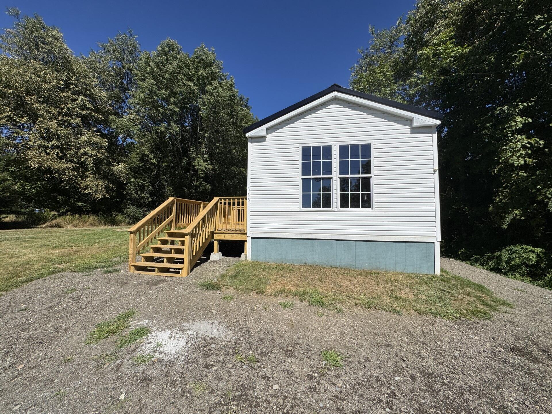 White-sided home with a wooden stairway and deck, set beside a wooded yard.