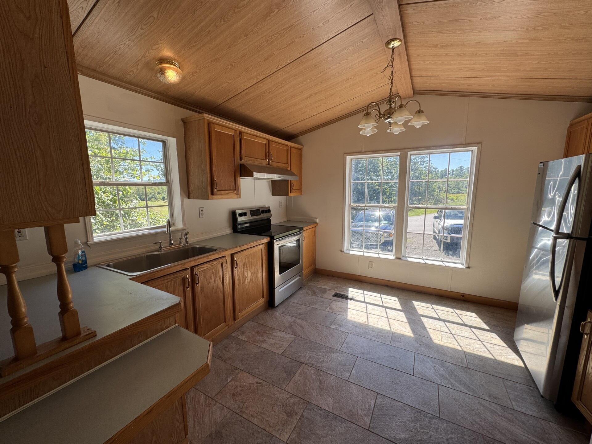 Kitchen with wood cabinets, a sloped wood ceiling, stainless appliances, and sunlight across the tiled floor.