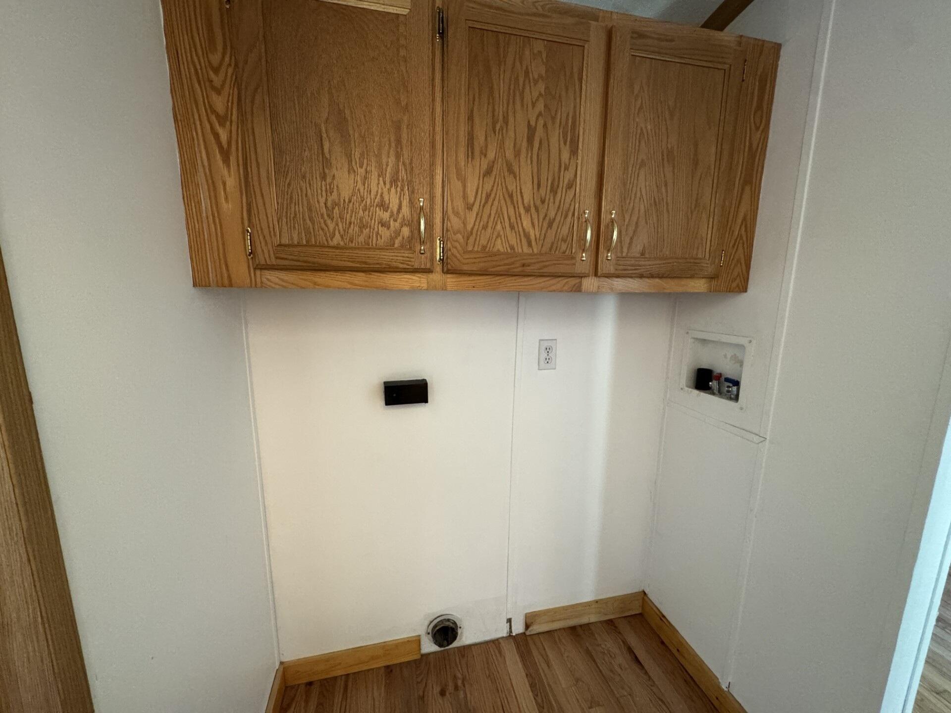 Laundry area with oak cabinets, washer hookups, and a floor drain.