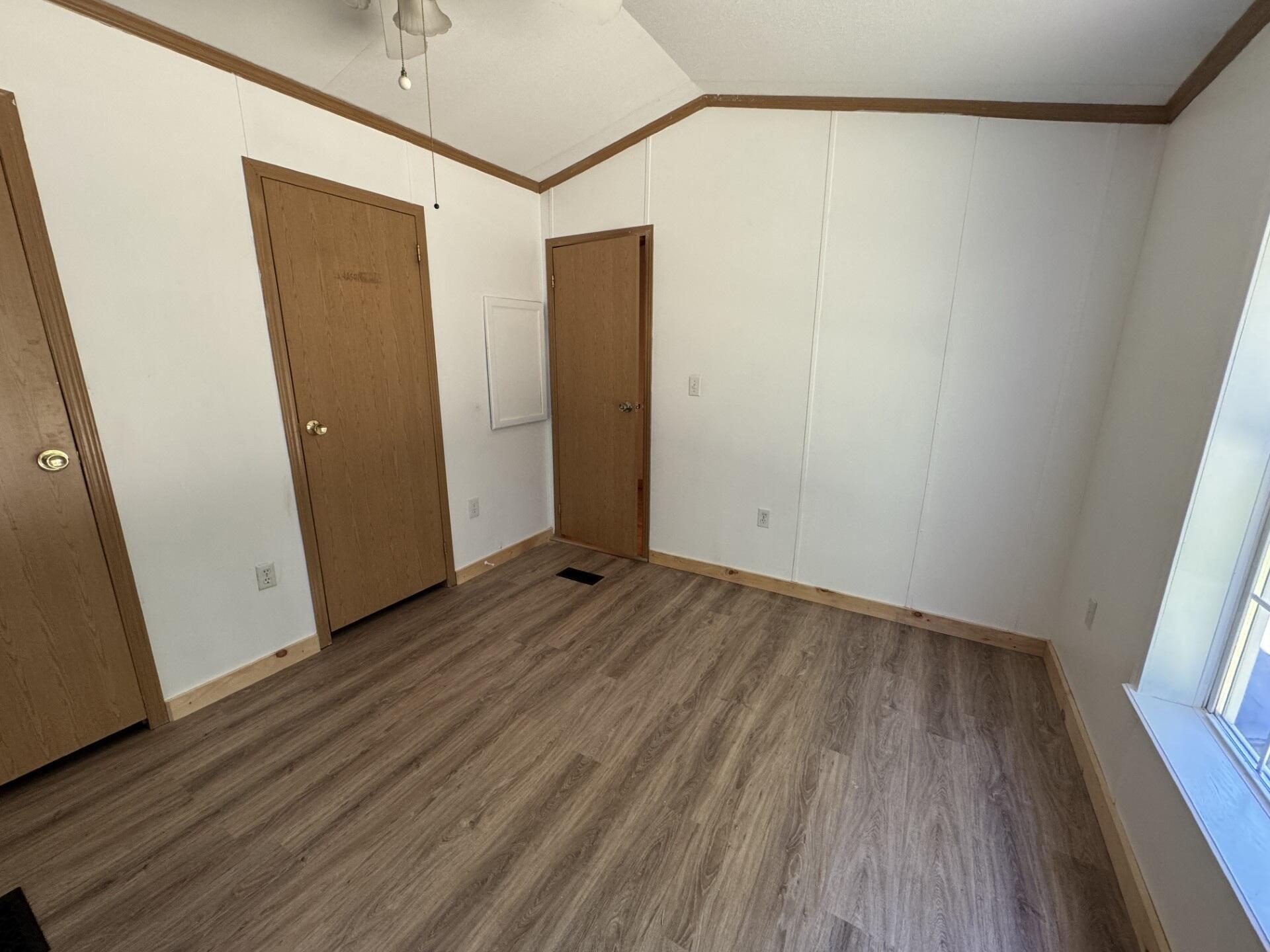 Empty room with plank flooring, three wooden doors, and a tall window.