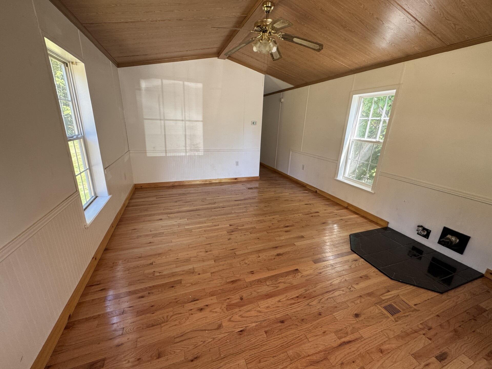 Empty room with hardwood floors, vaulted wood ceiling, and black tiled hearth.