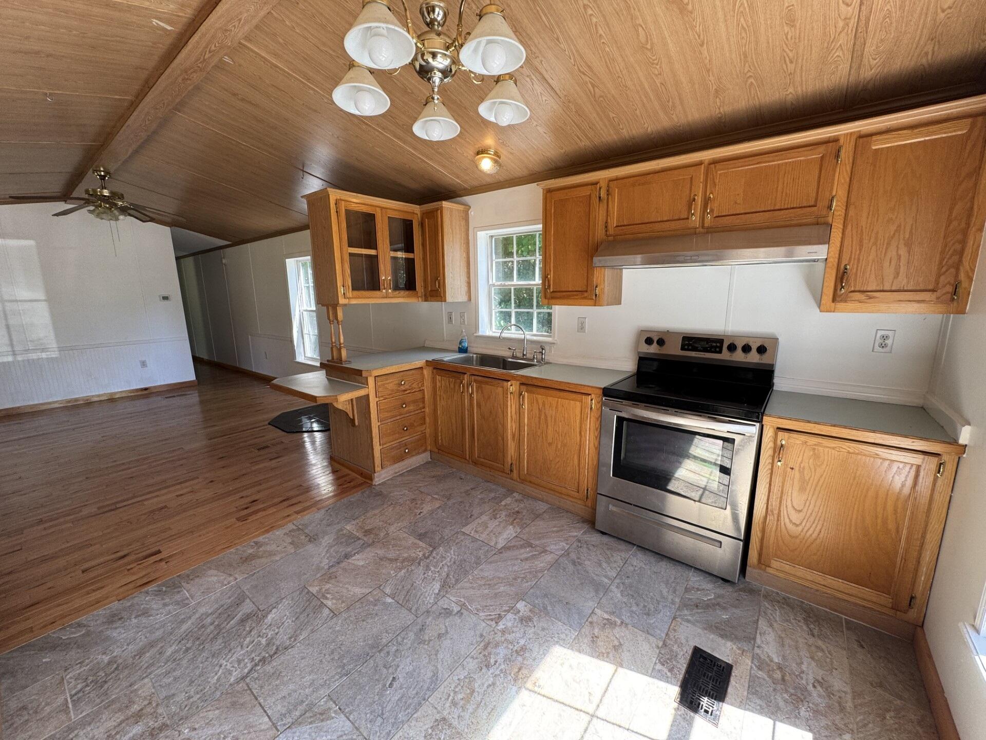 Kitchen with wood cabinetry and ceiling, tiled floor, stainless range, and an open adjoining room.