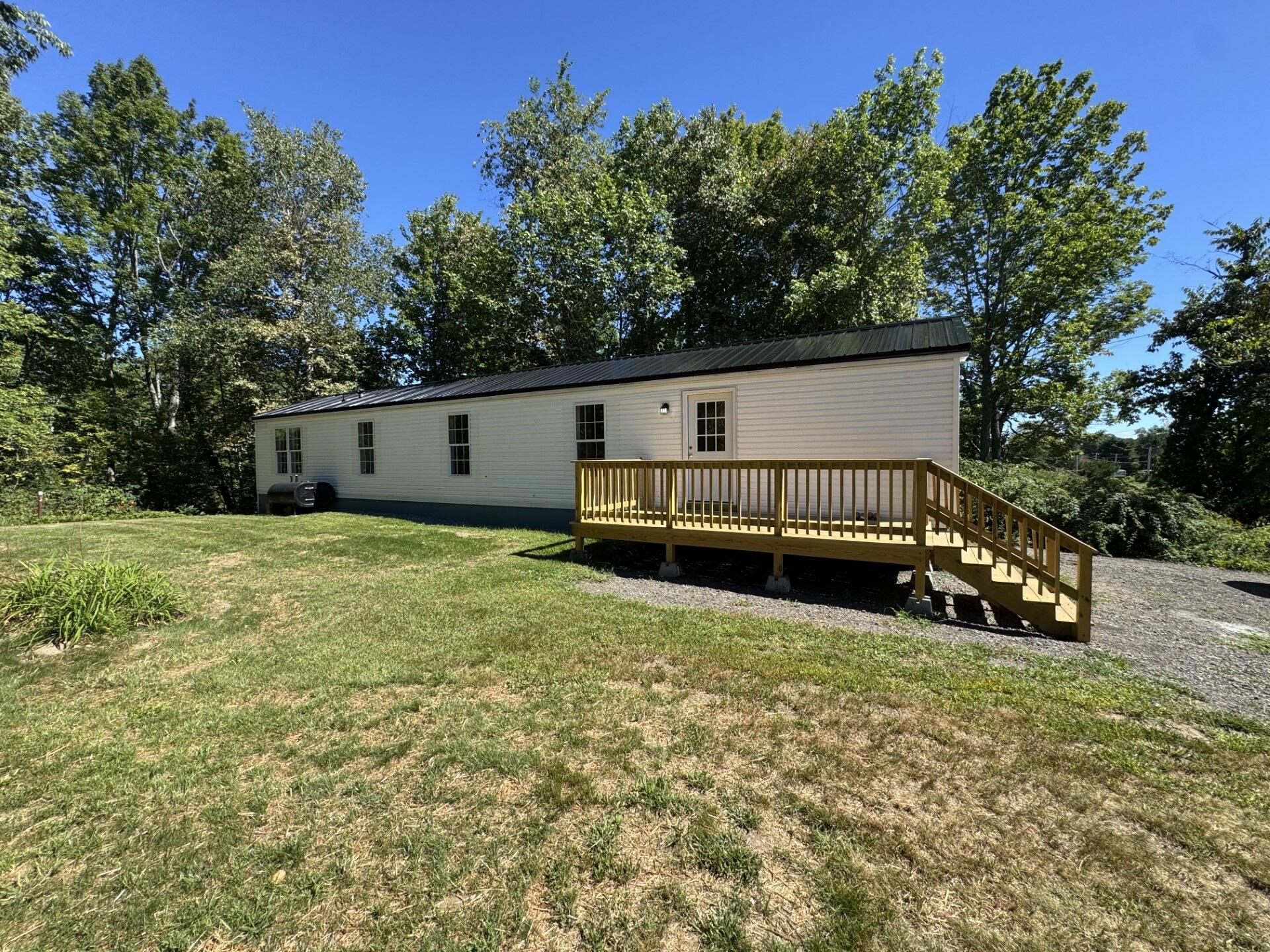Single-story home with a raised wooden deck and stairs in a tree-lined yard.