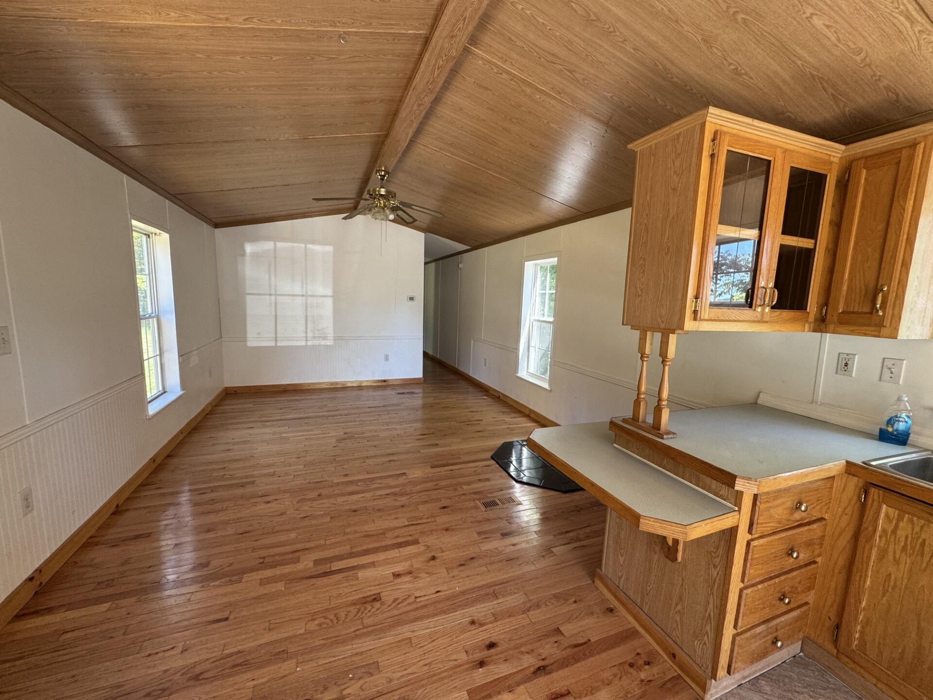 Mostly empty room with vaulted wood ceiling, hardwood floors, and built-in kitchen counter.