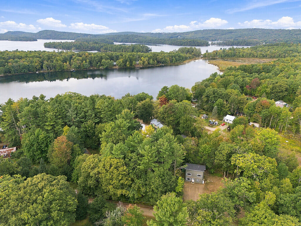 Aerial view of a wooded lakeshore home beside a broad lake and forested hills.