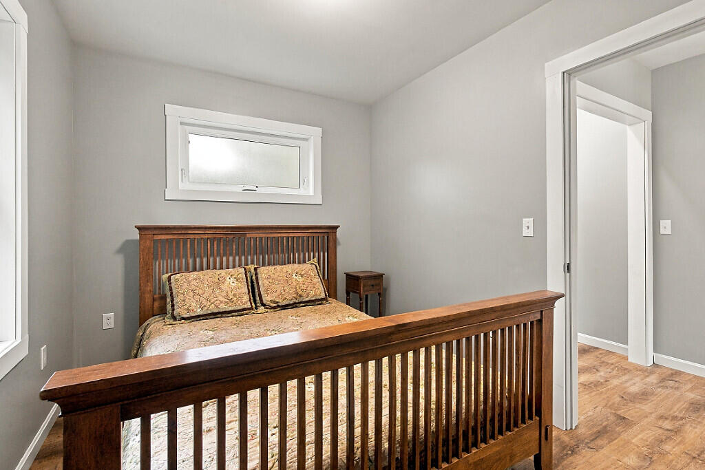 Bedroom with a dark wood bed frame, patterned bedding, gray walls, and wood flooring.