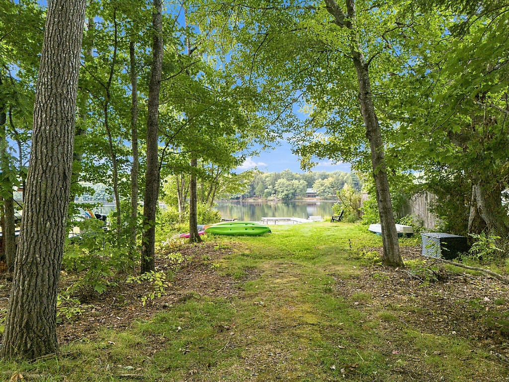 Wooded lakeside yard with kayaks on the grass and a small dock by the water.