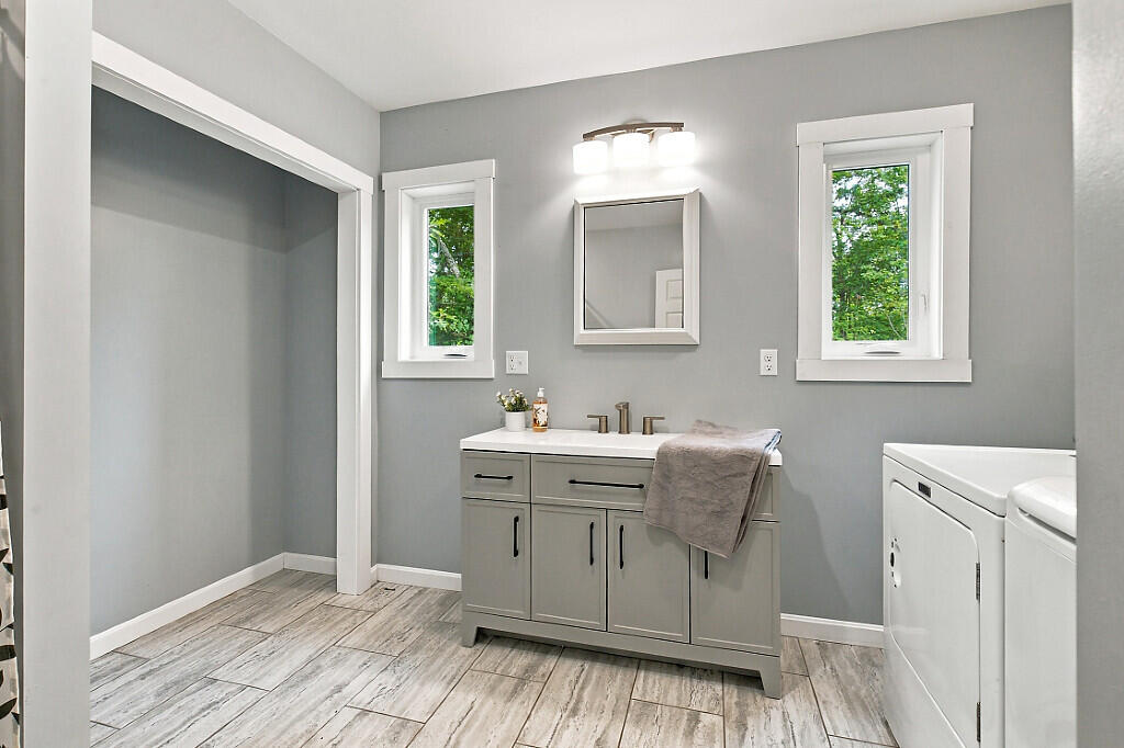 Bathroom with gray vanity, two windows, and white laundry appliances.