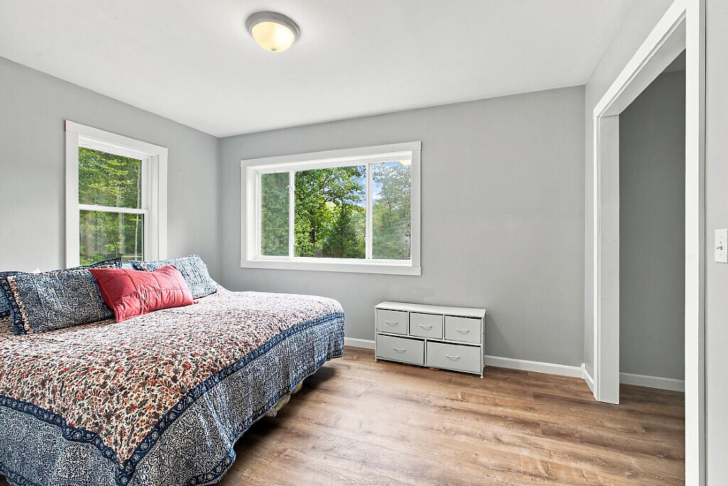 Bedroom with a patterned bedspread, gray walls, and windows overlooking trees.