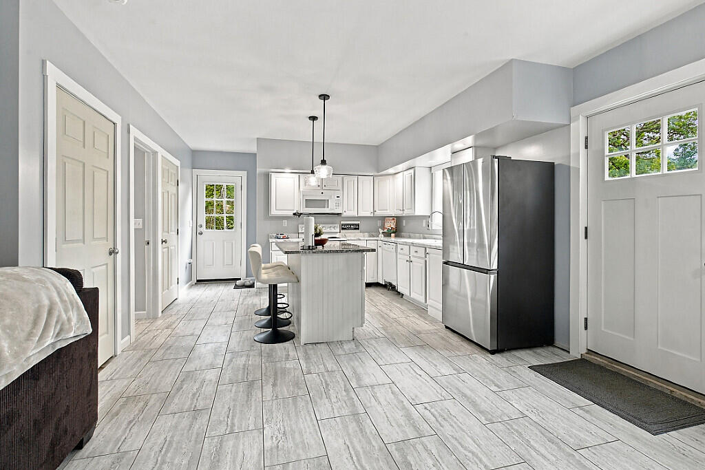 Kitchen with a white island, bar stools, stainless steel appliances, and large gray tile floors.