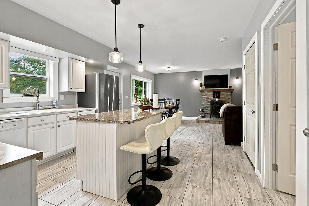 Open-plan kitchen with a stone-topped island, two bar stools, and a living room fireplace beyond.
