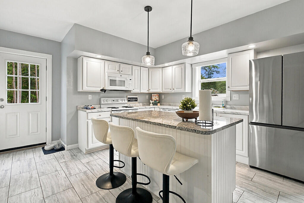 White kitchen with a granite island, three bar stools, and stainless steel appliances.