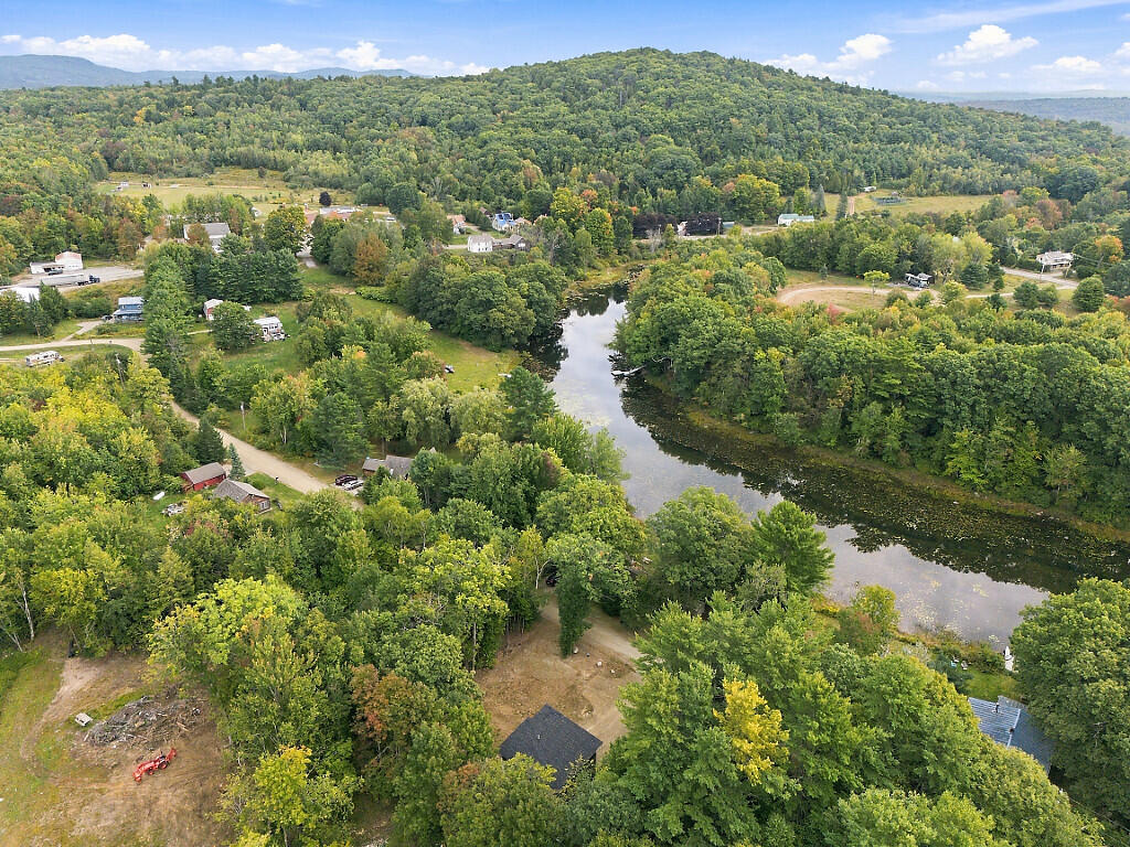 Aerial view of homes among autumn-colored trees beside a winding river and forested hills.