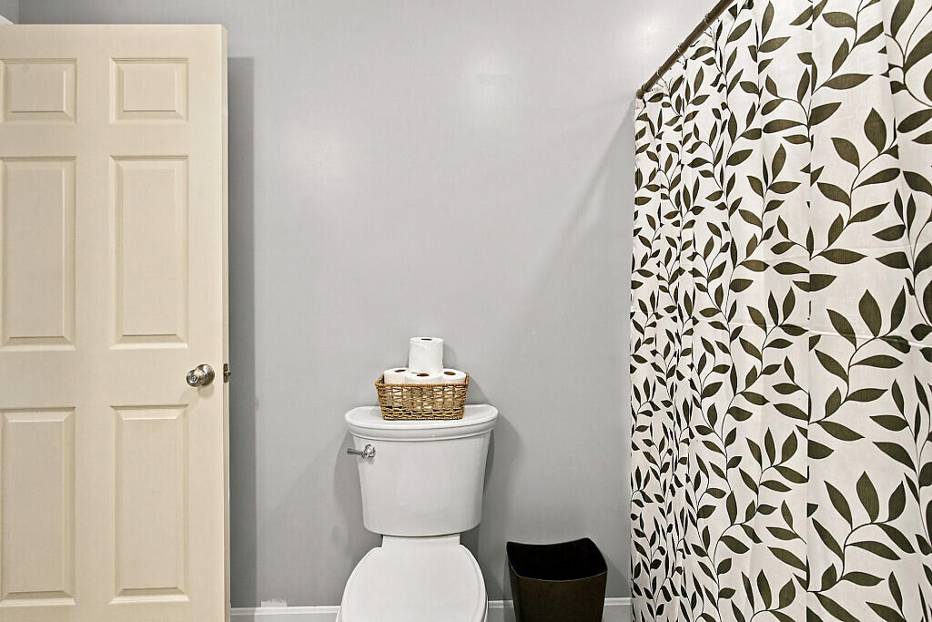 Bathroom with a white toilet and a leaf-patterned shower curtain.