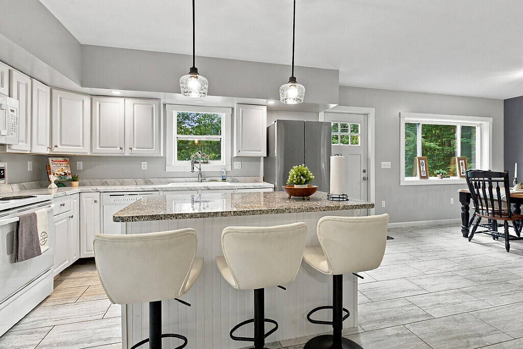 Kitchen with white cabinets, stainless appliances, and a granite island with three upholstered stools.