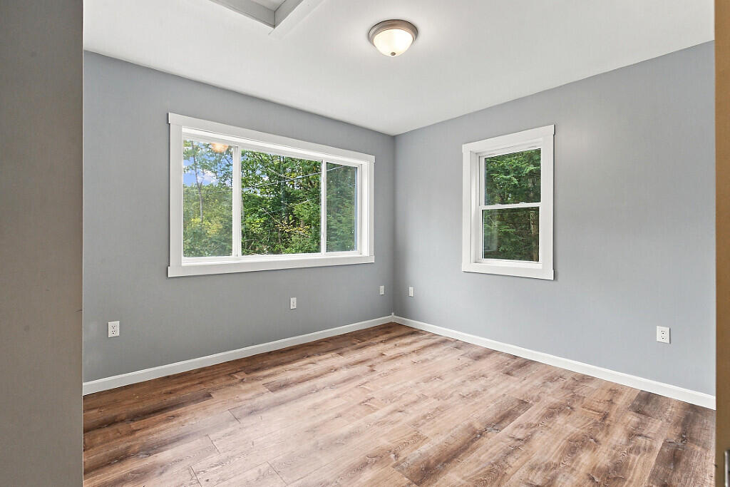 Empty bedroom with gray walls, wood-look flooring, and two windows facing trees.