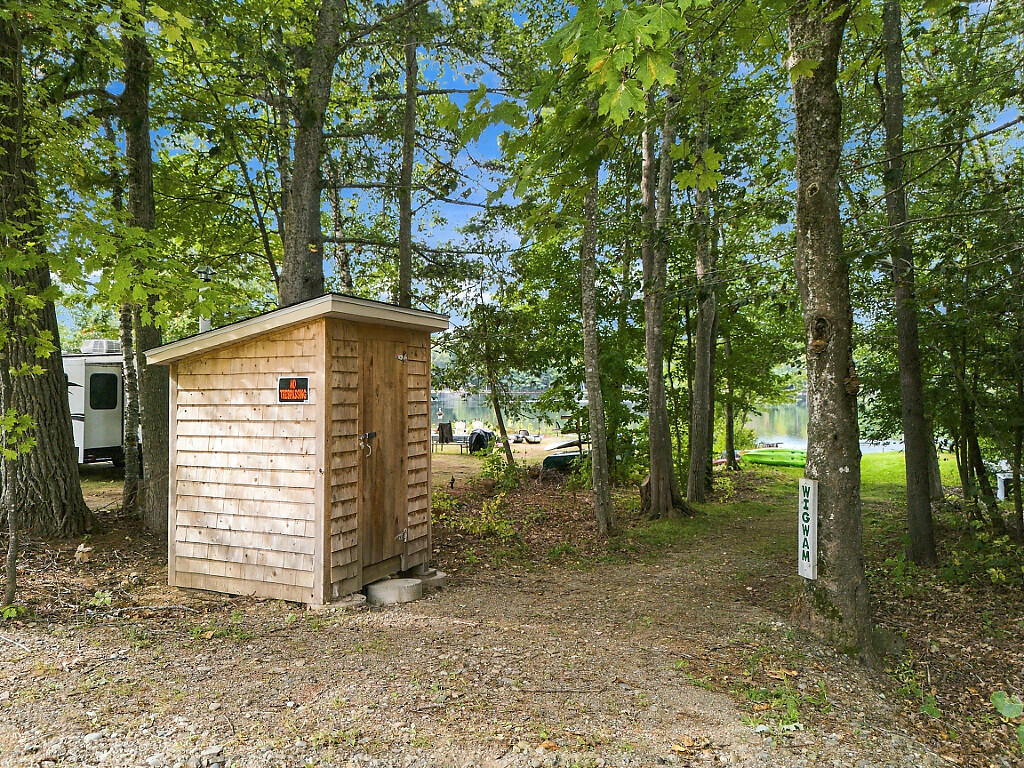 Wooden shed among lakeside trees, with a small dock and green kayaks visible beyond.