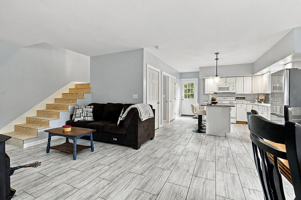 Open living room with dark sofa and wooden staircase adjoining a bright white kitchen.