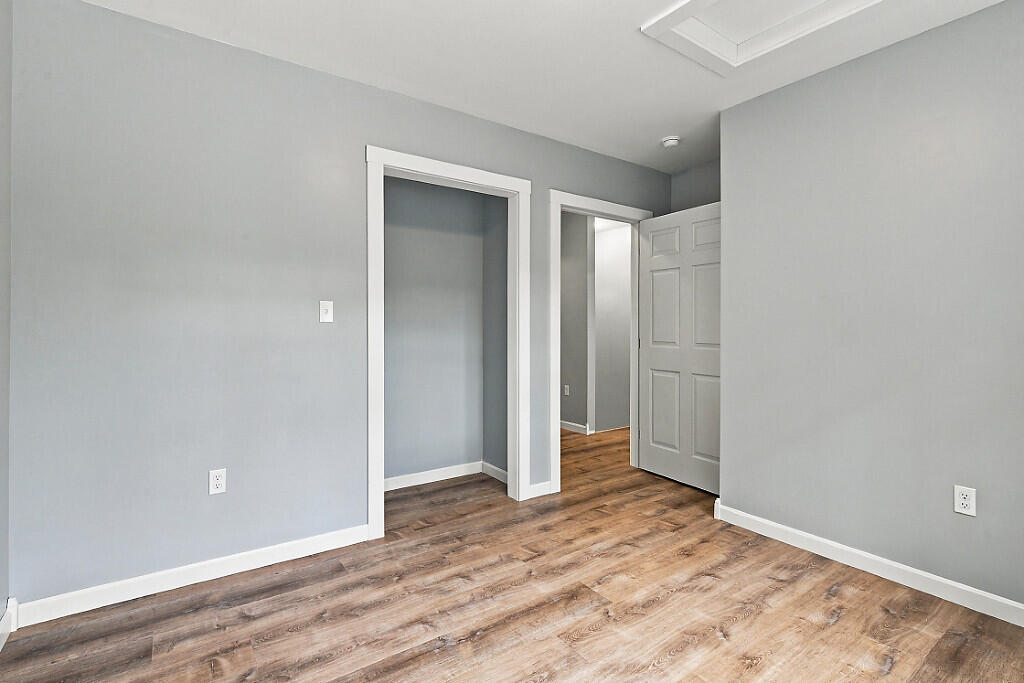 Empty room with gray walls, wood-look flooring, and open doorways.
