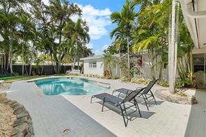 Outdoor pool beside a paved patio with lounge chairs and tropical landscaping.