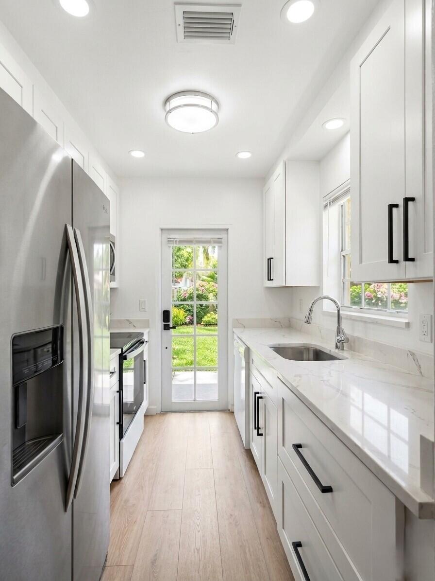 Bright white kitchen with stainless steel appliances, marble-look counters, and a glass-paneled garden door.