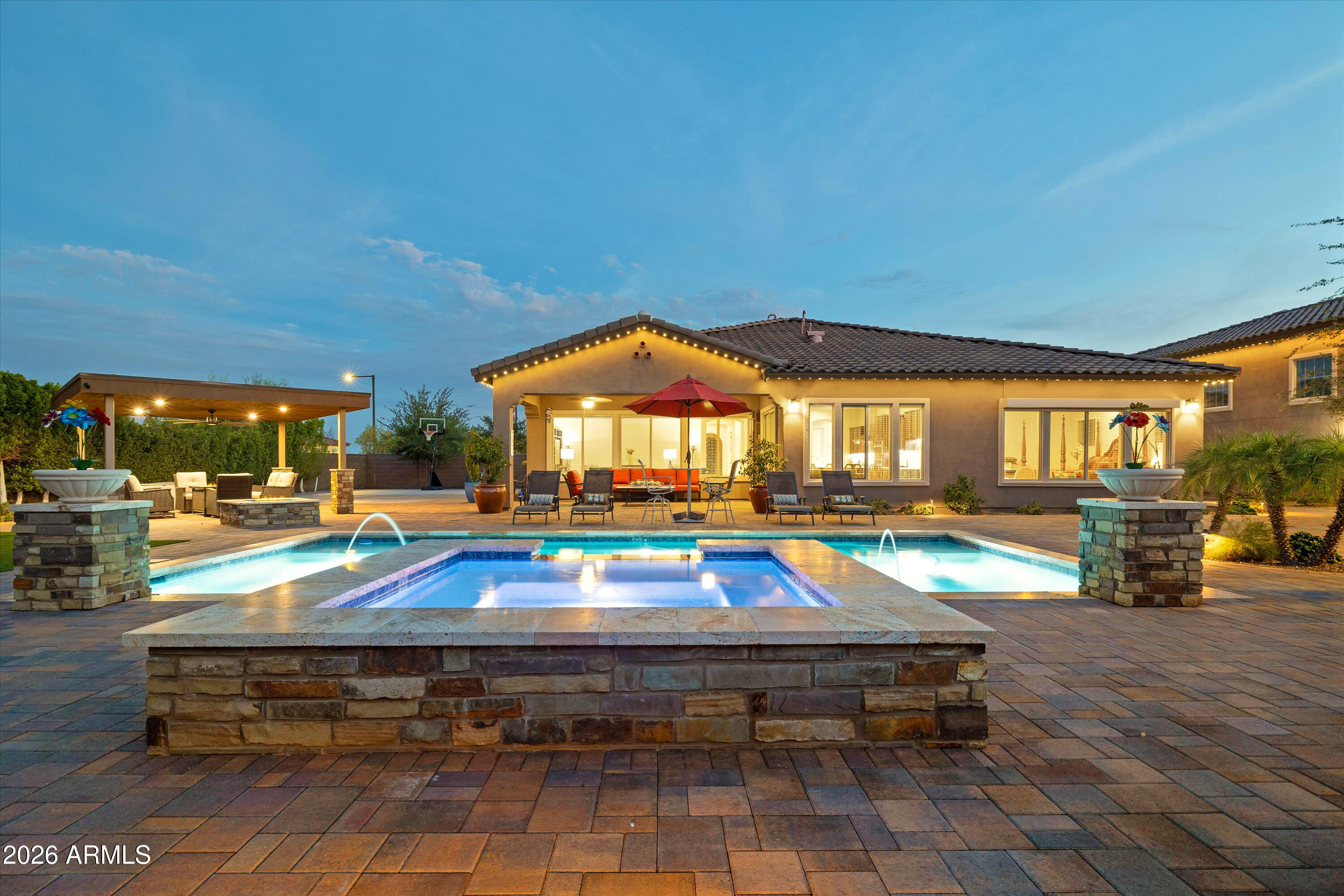 Backyard pool and raised stone spa beside a lit patio with seating and a covered pergola.