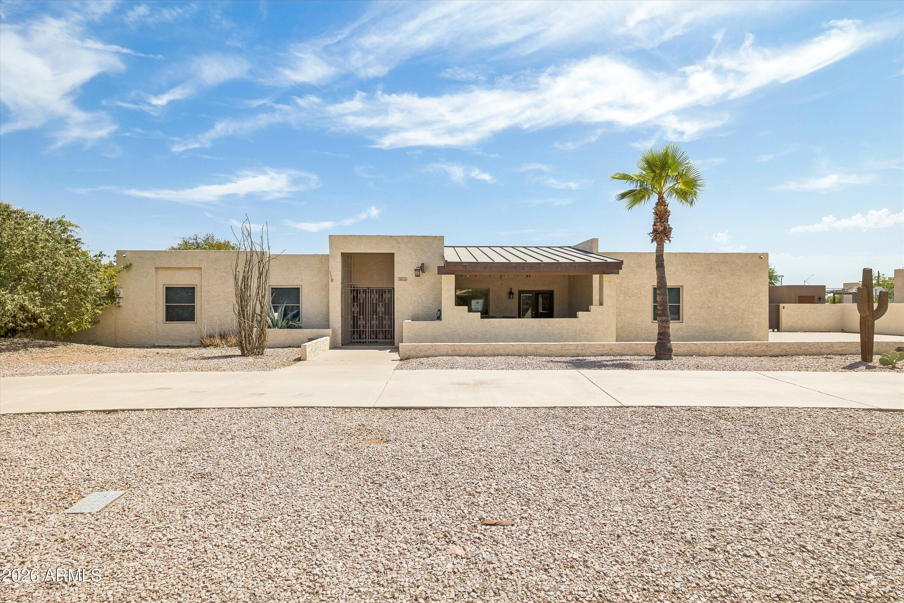 Single-story stucco home with a covered entry, gravel yard, palm tree, and saguaro cactus.