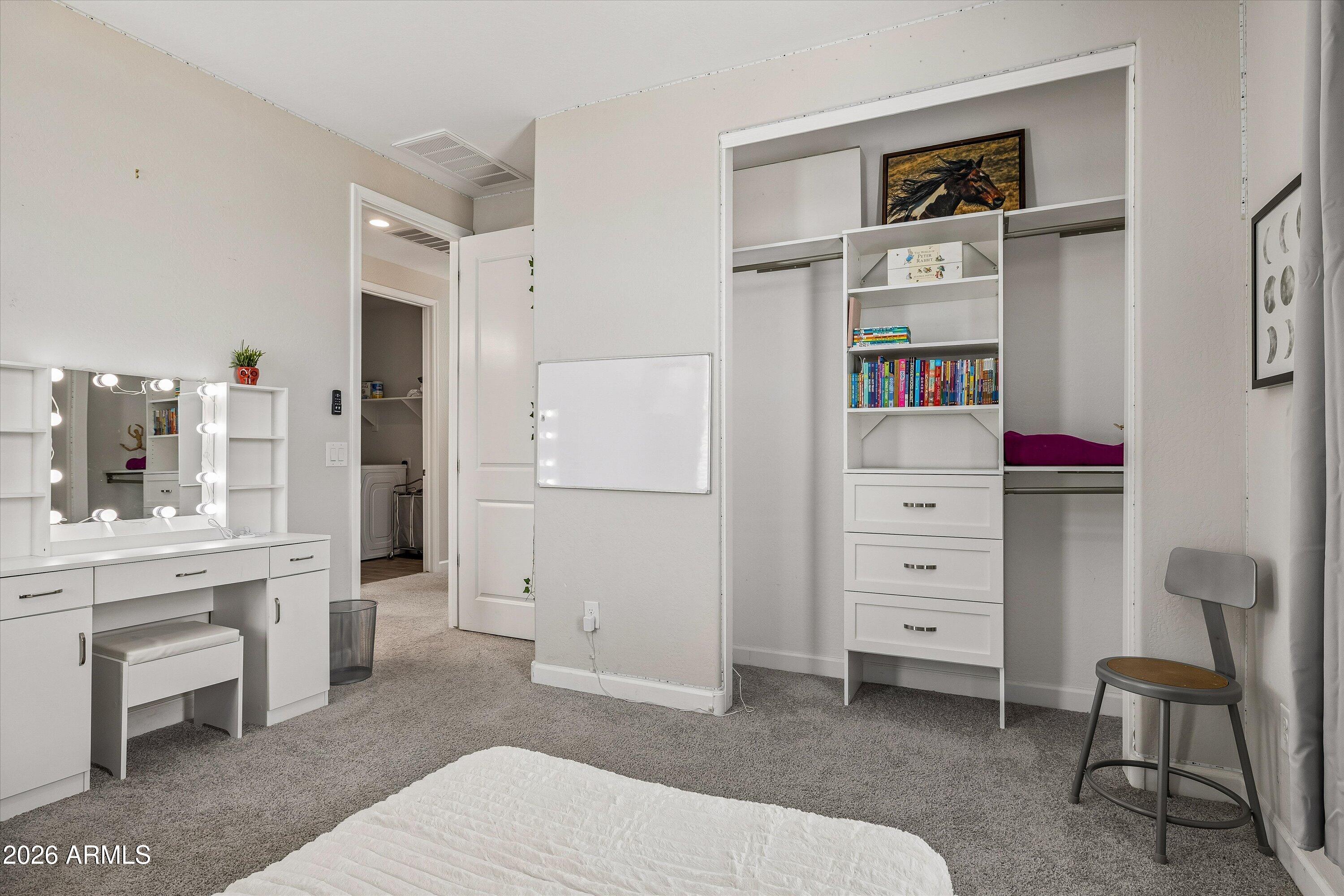 Bedroom with a lit vanity and open built-in closet displaying books.