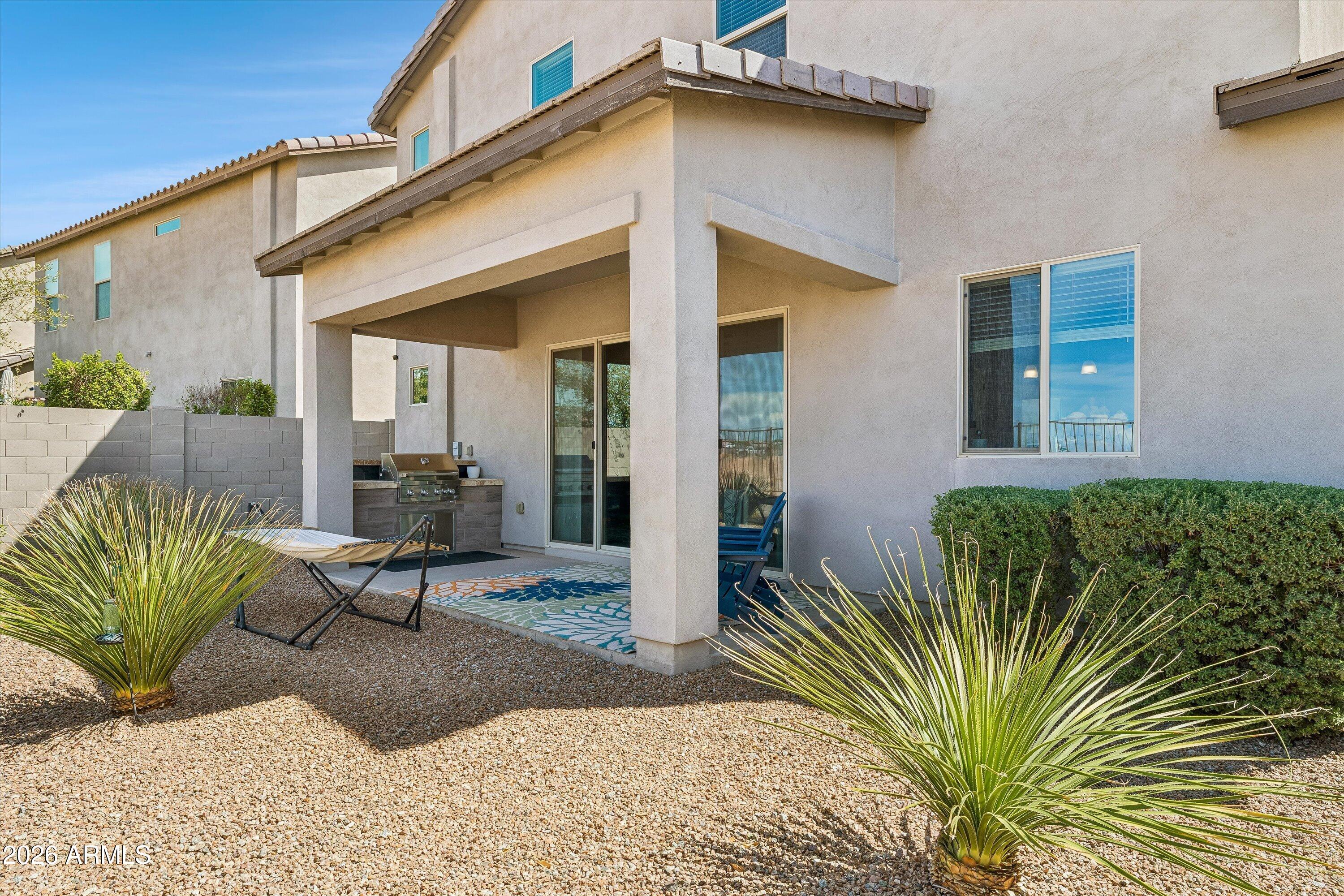 Rear patio of a two-story stucco home with covered seating, outdoor grill, and gravel landscaping.