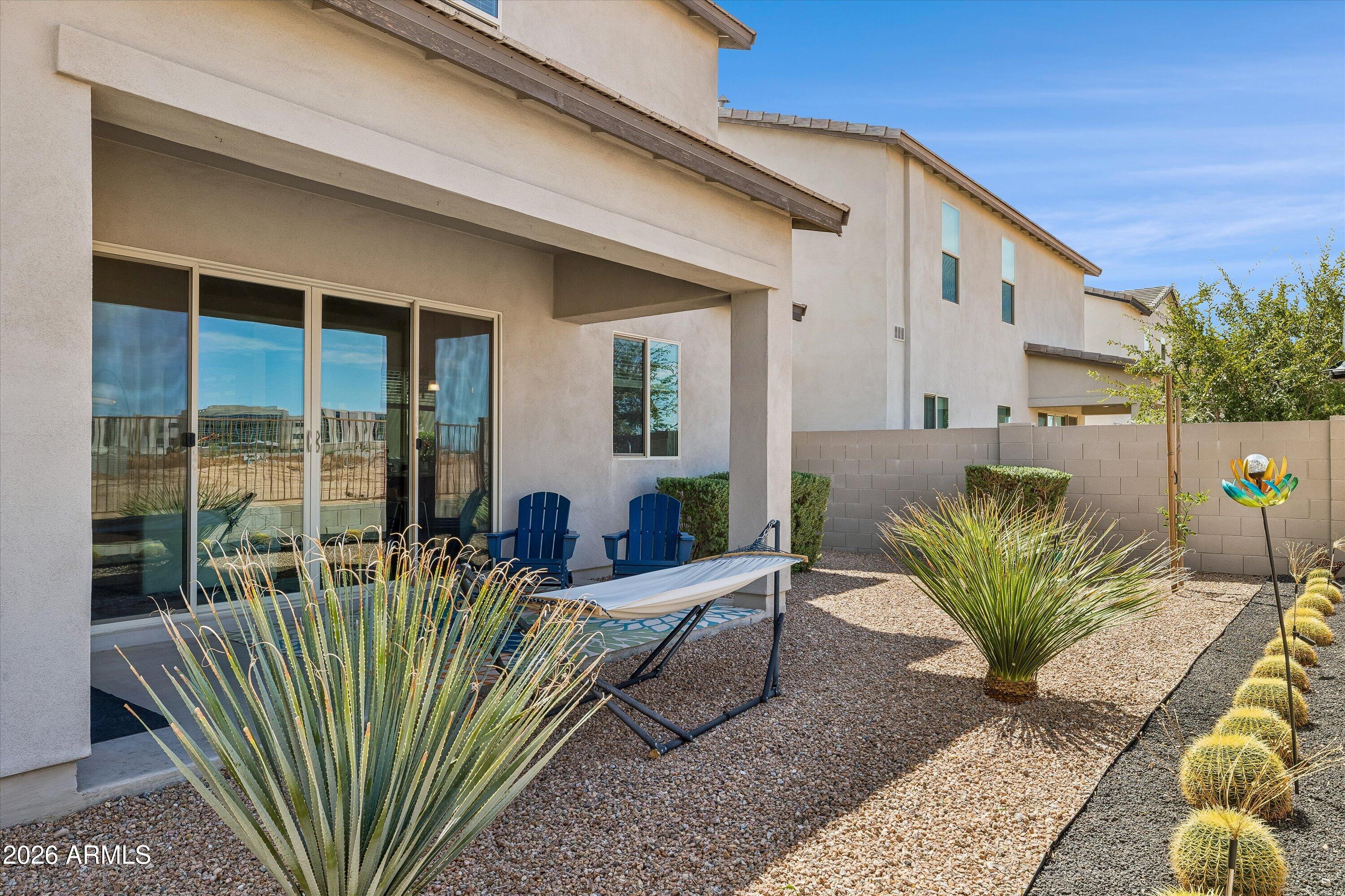 Desert backyard patio with a hammock, blue chairs, gravel landscaping, and sliding glass doors.