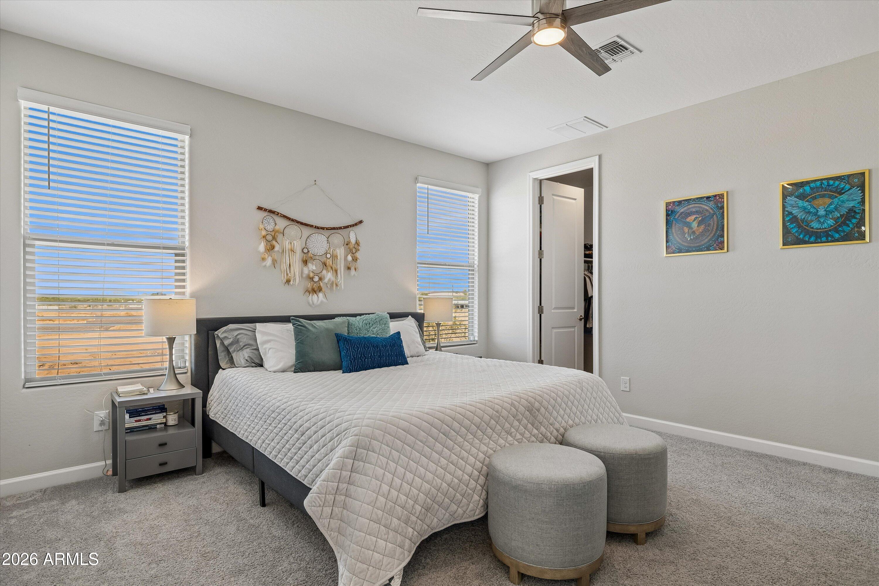 Furnished bedroom with a large bed, teal pillows, ceiling fan, and desert views through two windows.