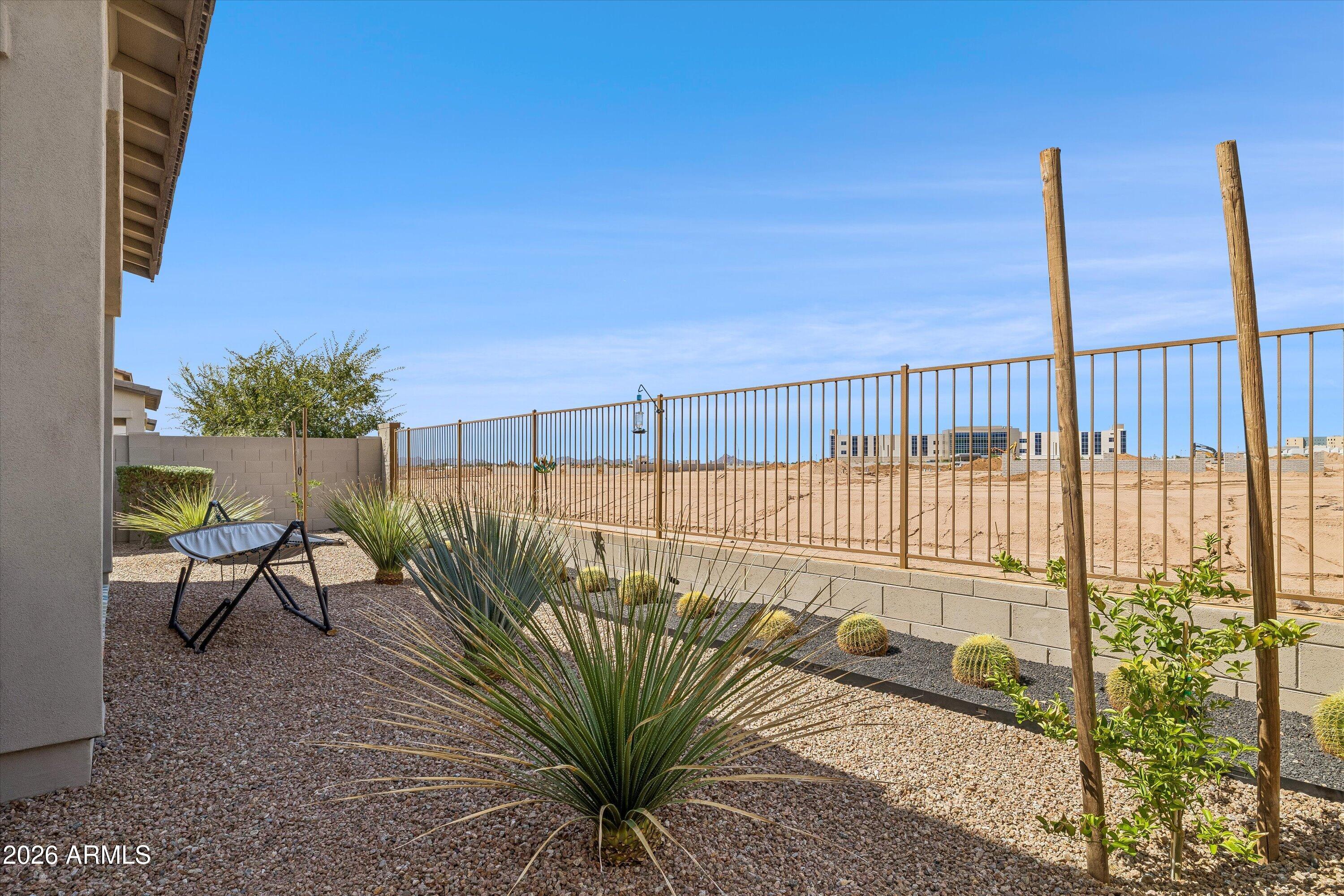 Gravel backyard with desert plants and a hanging chair beside a metal fence overlooking open land.