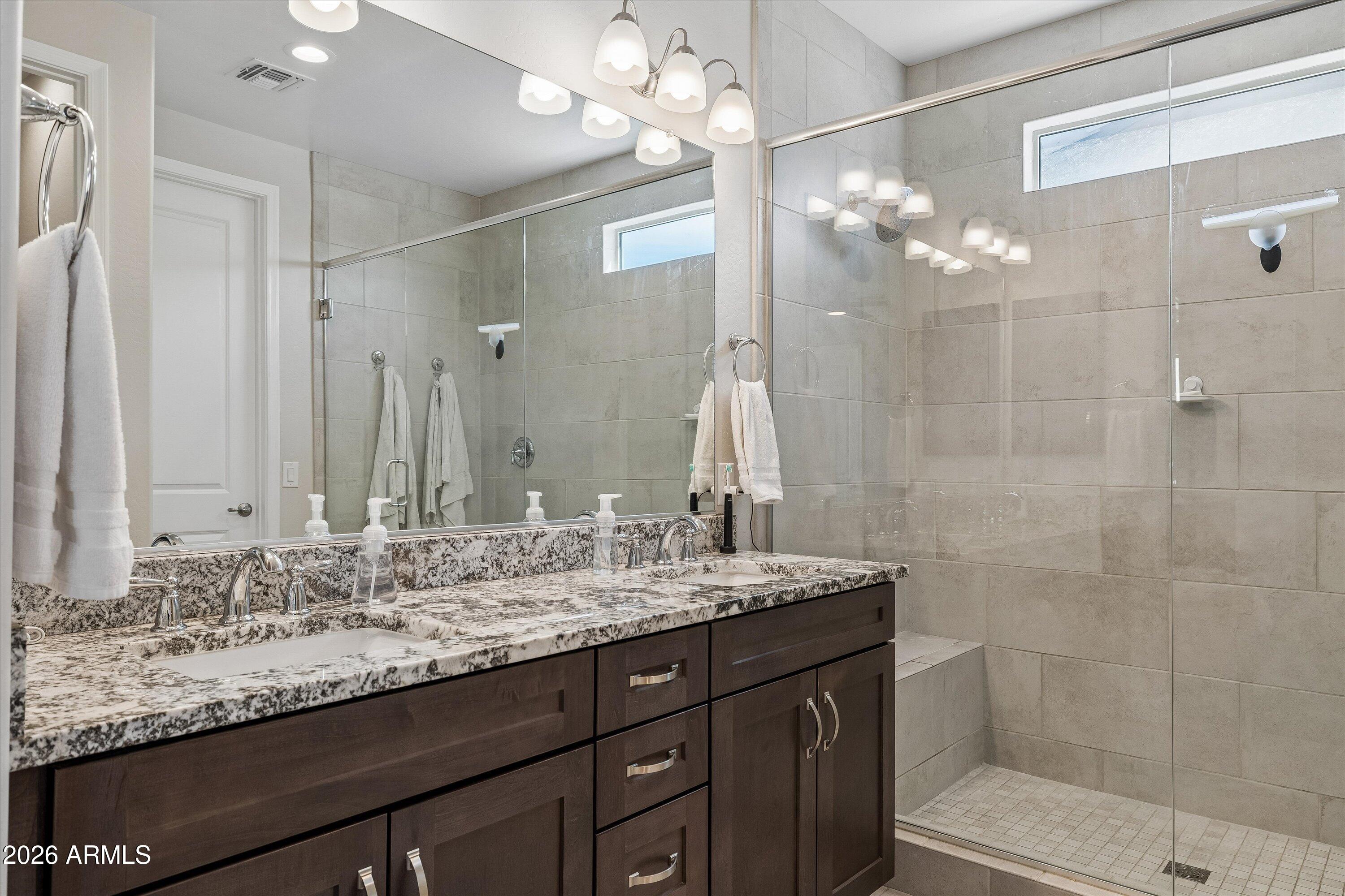 Bathroom with a dark double vanity, speckled stone countertop, and spacious glass-enclosed tiled shower.