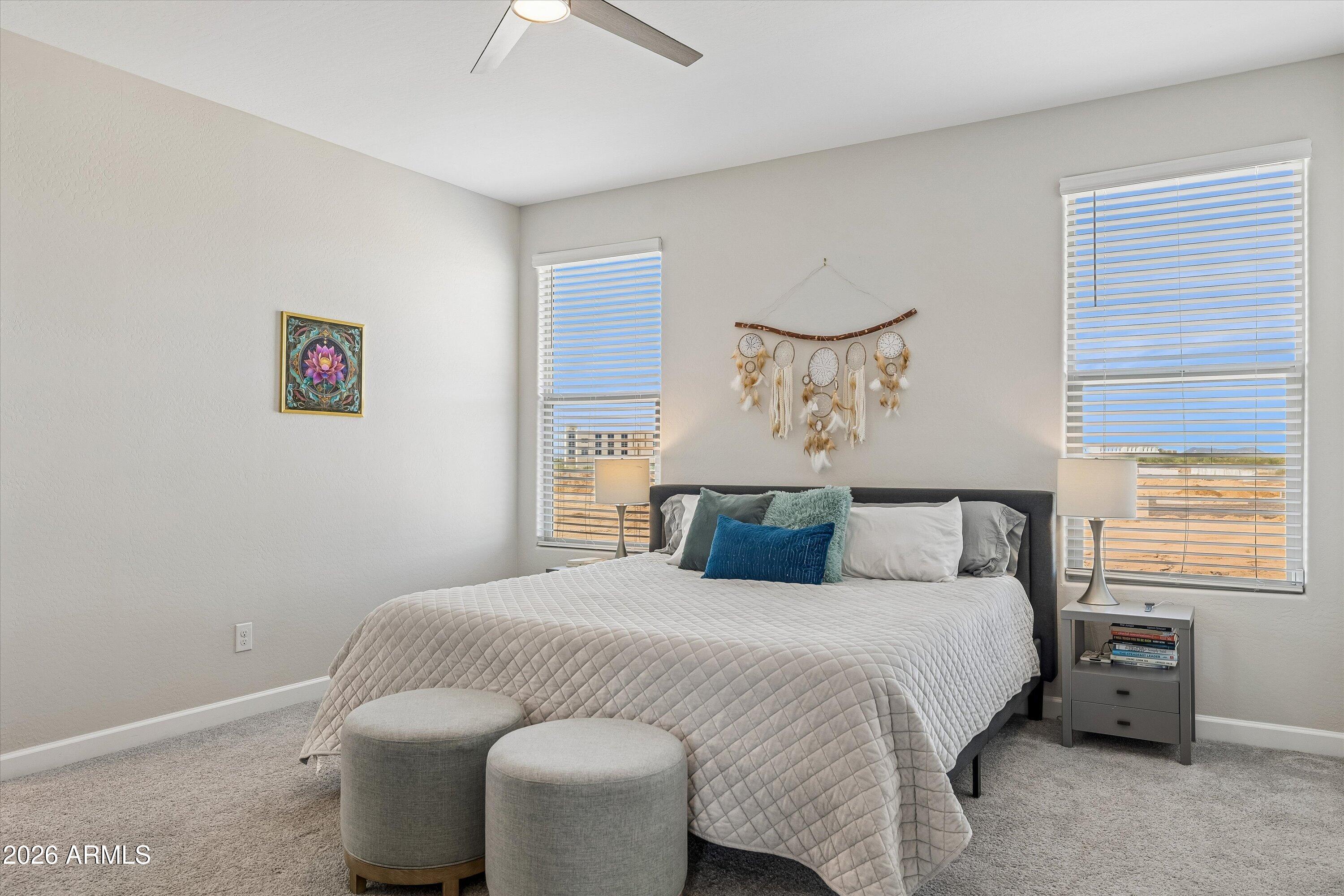 Furnished bedroom with a large bed, two round stools, and windows overlooking an arid landscape.